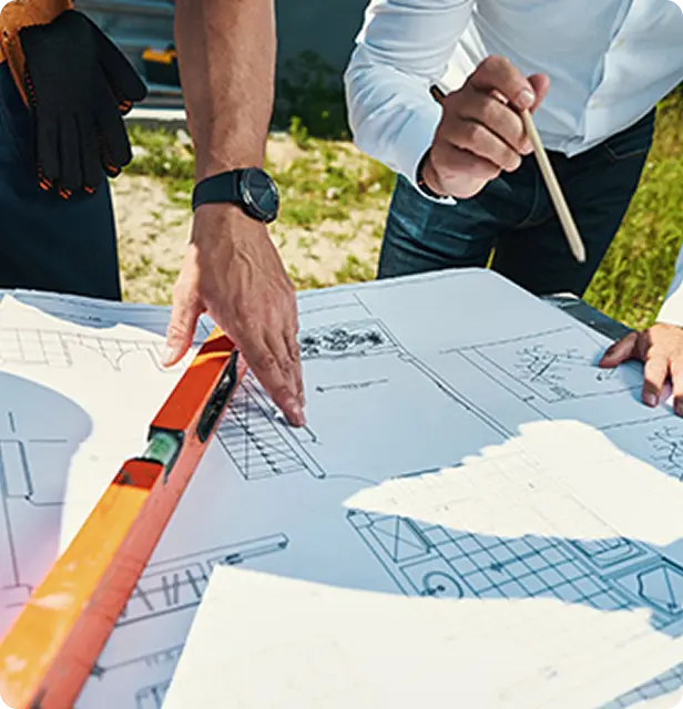 Close-up of architects reviewing blueprints with level tool and pencil during outdoor planning meeting