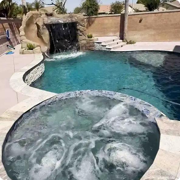 Luxury swimming pool with rock waterfall and bubbling hot tub in sunny backyard