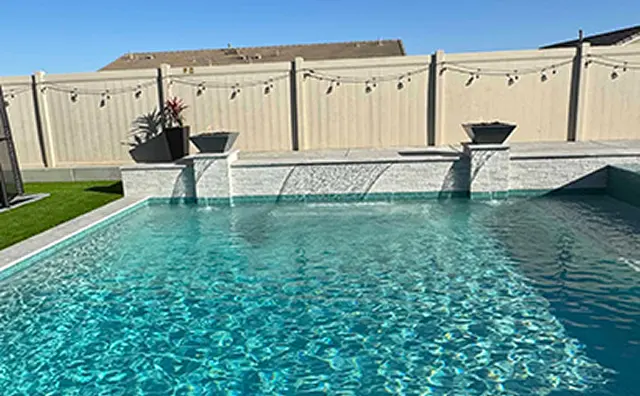 Sparkling clear swimming pool with sleek water feature and potted plants against a privacy fence
